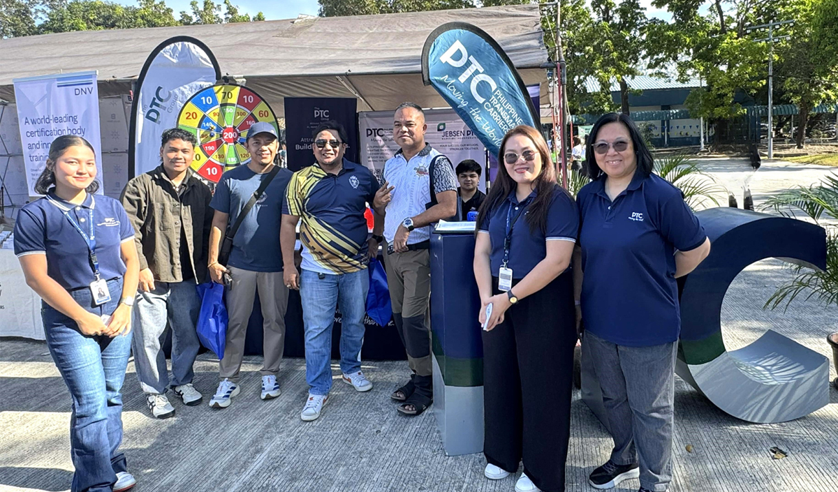 Eight people stand together at an outdoor booth featuring DTC banners and a colorful prize wheel in the background.