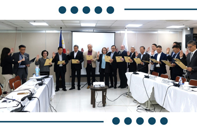 Group of professionals in suits stand in a conference room, each holding a document, as if receiving certificates at a ceremony with flags in the background.