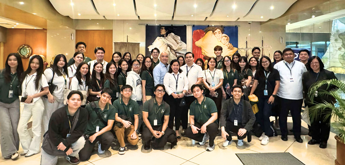 Far Eastern University Tourism students | PTC Group photo of a diverse team posing in a showroom lobby, many wearing green polo shirts and name badges, smiling at the camera.
