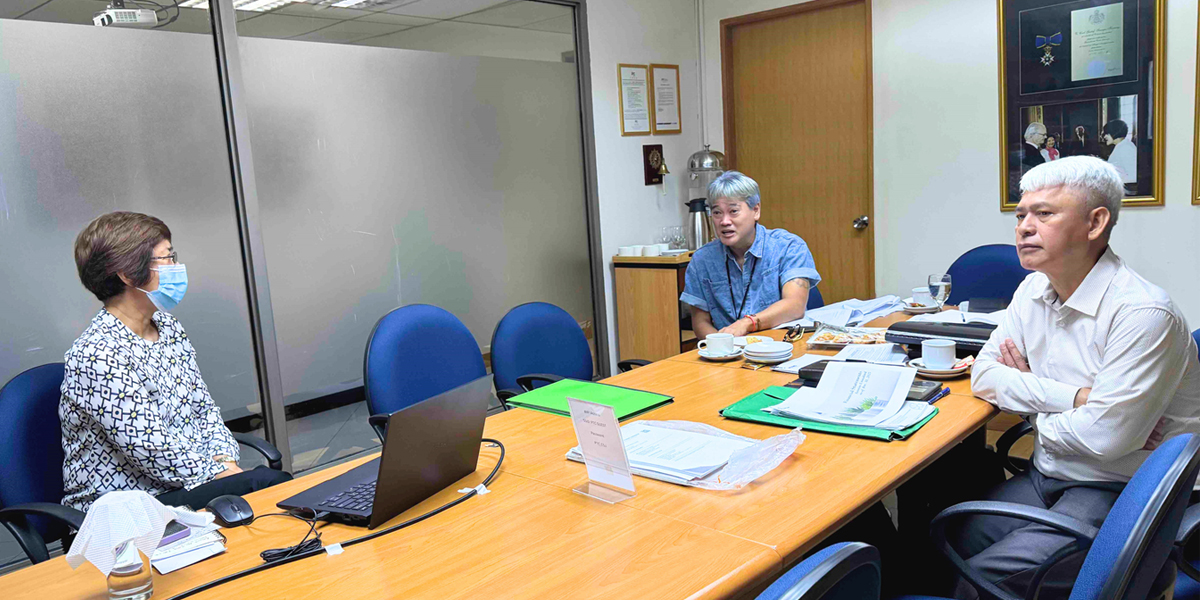 PTC-CSJ Foundation | PTC Three professionals in a conference room around a table; woman on the left wears a face mask, with a laptop and papers nearby and two men on the right staying engaged.