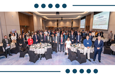 Group photo of conference attendees standing behind round tables in a large ballroom or conference hall.