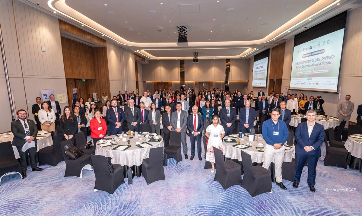 Group photo of a large professional conference audience in a banquet hall, around round tables with place settings and name badges visible.