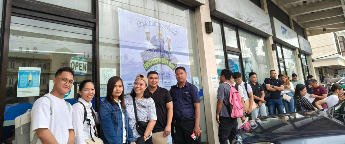 Group of people waiting in line outside a storefront, with a large window poster behind them and a car in the foreground.