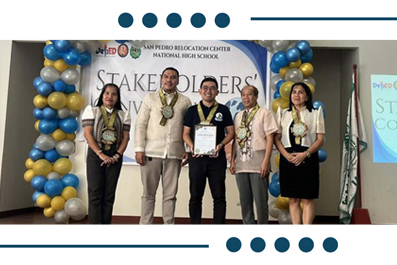 Group of five award recipients on a stage, wearing medals and sashes, with a certificate in the center during a school recognition ceremony.