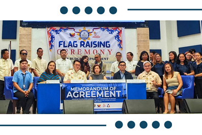 Group of officials and attendees posing on stage during a flag-raising ceremony, with a Memorandum of Agreement banner in front.