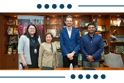 Four professionals stand together in an office, smiling for the photo with shelves of awards behind them.