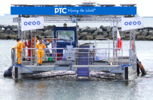 Floating service platform on the water with a blue canopy and railing; crew in orange coveralls on deck amid banners.