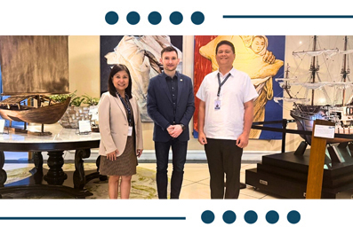 Four professionals pose in a museum exhibit about maritime artifacts, with model ships and large paintings.
