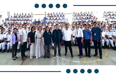 Group photo of students in white uniforms and staff standing together in a gymnasium, front row facing the camera.