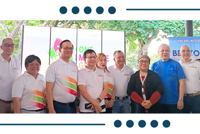 Group of people posing for a photo at an outdoor event, several wearing white shirts with colorful diagonal stripes, with banners in the background.