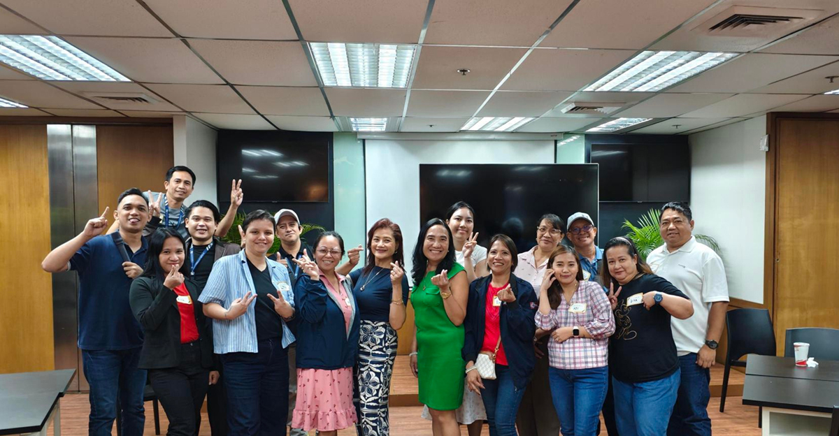 PTC FCR holds seminar-2 | PTC Group of coworkers posing for a photo in a bright office meeting room, many smiling and showing peace signs, with a large screen behind them.