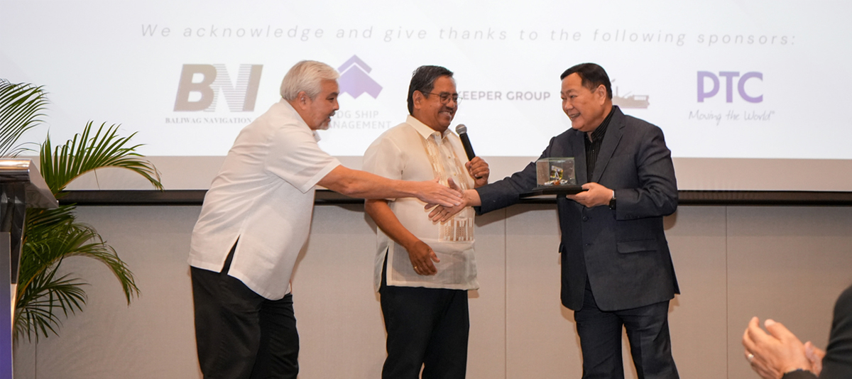 PTC reinforces industry-2 | PTC Three men on a stage shake hands as one receives a glass award from a colleague with a microphone nearby.