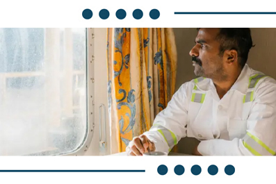 Man in a white safety shirt with reflective stripes sits by a window, looking outward thoughtfully.