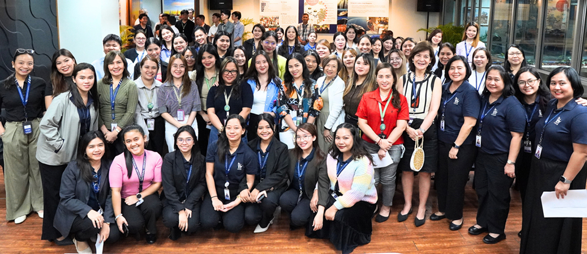 Group of people posing for a photo at a workplace event or conference in an office lobby. They wear name badges and look at the camera.",