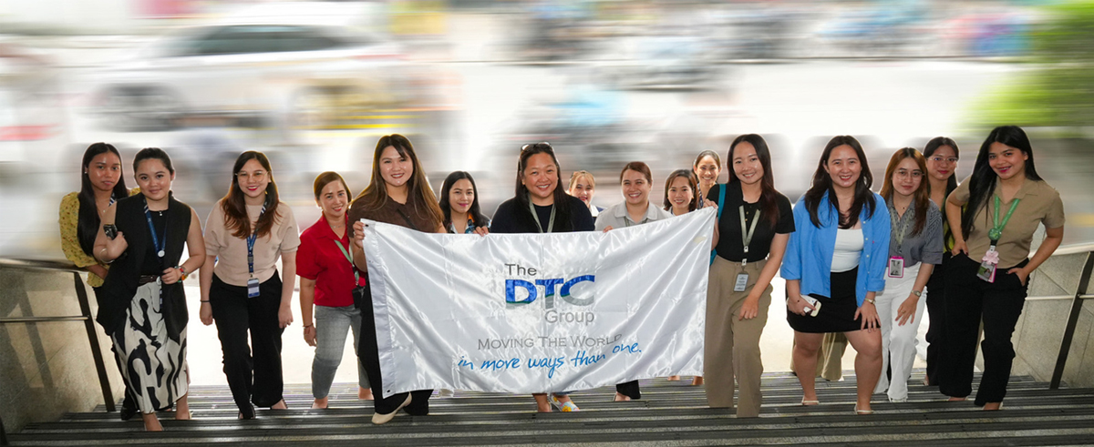 Diverse group of women standing on stairs, holding a banner that reads The DTC Group.