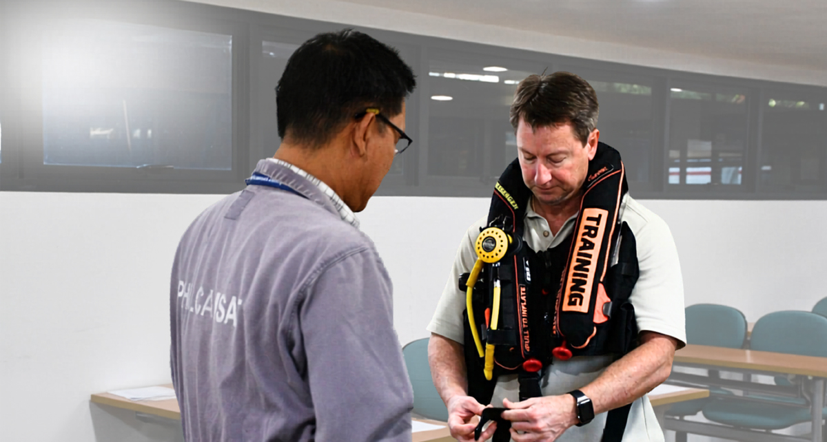 Dry CA-EBS Training-2 | PTC Two men in a training room; one wears a bright safety vest labeled TRAINING and examines gear while the other watches.