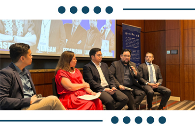 Five panelists seated in a conference panel discussion on stage with a projection screen behind them.