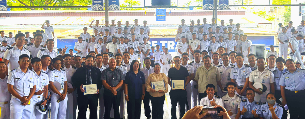 Large group of cadets in white uniforms posing for a group photo under a covered area, several adults in front holding certificates.