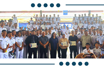 Group of students in white uniforms posing with certificates and officials at a ceremony on stage.