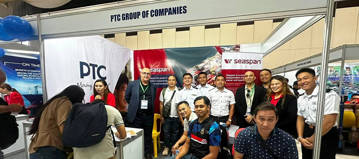 Group of professionals posing at a trade show booth labeled 'PTC Group of Companies' with banners for Seaspan and PTC nearby.