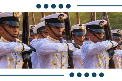 Line of soldiers in white ceremonial uniforms marching with rifles in a parade.