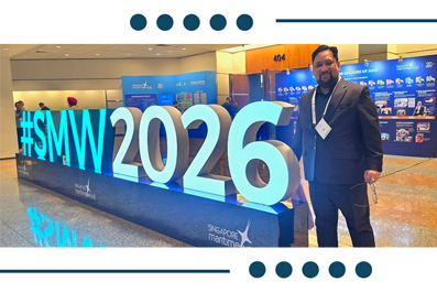 Man in a suit standing next to a large illuminated sign reading '#SMW 2016' at a conference hall.