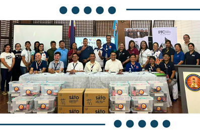 Group of people standing behind tables stacked with donation boxes at a community charity event, indoors.