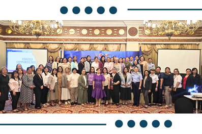 Group of about 40 professionals in business attire posing for a formal group photo in a ballroom conference room with a blue backdrop and screens.