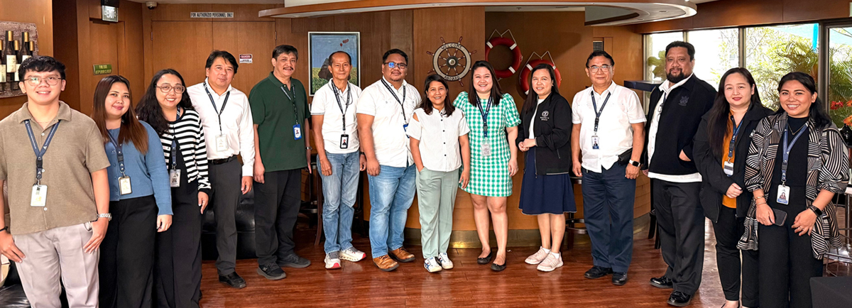 PHILCAMSAT advances digital maritime training-2 | PTC Group of diverse colleagues posing together indoors for a photo in a ship-themed room, wearing name badges and lanyards.