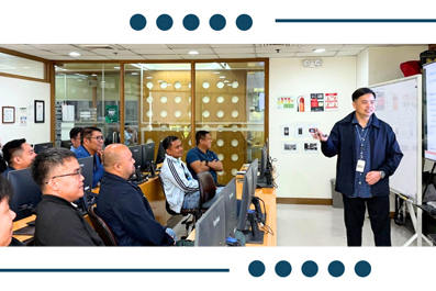 Instructor presents to adults in a computer lab; attendees sit at desks with monitors, listening attentively.