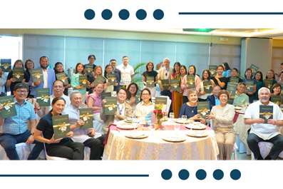 Group of about 30 people posing for a photo at a banquet, many holding black booklets, with a round table and cake in the center.