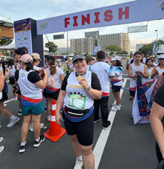 17th FAME Fun Run 2026-5 | PTC Runner with bib and medal crossing the finish line under a FINISH banner as spectators cheer.