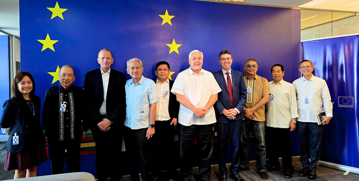 European Union Delegation-3 | PTC Group of ten adults in smart casual attire posing for a photo in front of a blue European Union banner with yellow stars.