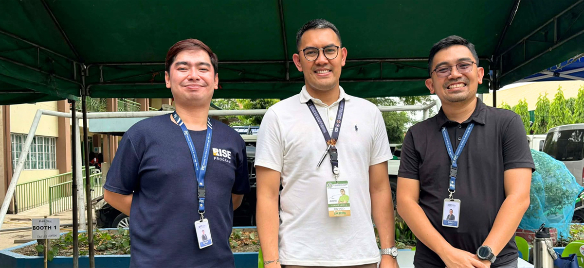 PTC RISE Program-2 | PTC Three men with lanyard badges standing under a green canopy at an outdoor event panel.