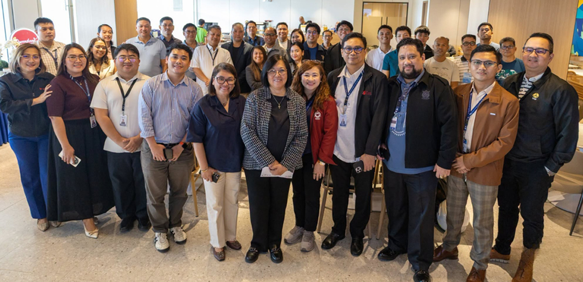 Large diverse group of coworkers posing for a group photo in a conference room, many wearing ID badges.