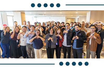 Diverse group of coworkers in an office lobby smiling and forming heart shapes with their hands.