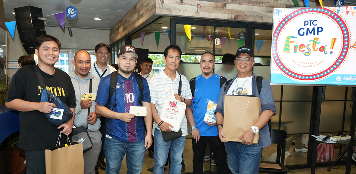 PTC marks Day of the Seafarer 2026-2 | PTC Group of men posing for a photo at a festival event, some holding bags and packages in front of a festival sign.