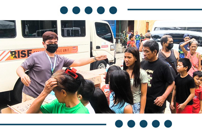 People in line beside a white van as aid distribution takes place; a man in a gray shirt gestures toward the queue while others wear masks.