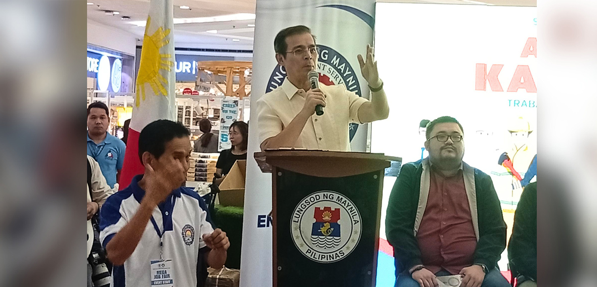 joins Kalayaan Job Fair 2026 | PTC Man in a light shirt speaks into a microphone at a podium bearing the Manila city seal, with the Philippine flag nearby.