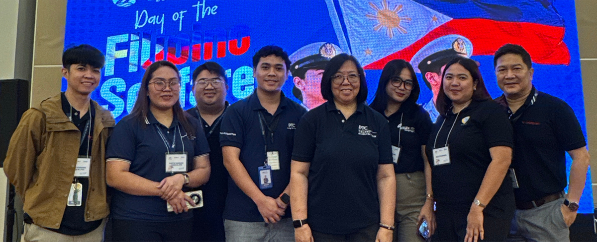 Eight professionals posing for a group photo at a conference, with a bright blue backdrop featuring a Philippines flag motif behind them and their name badges visible.