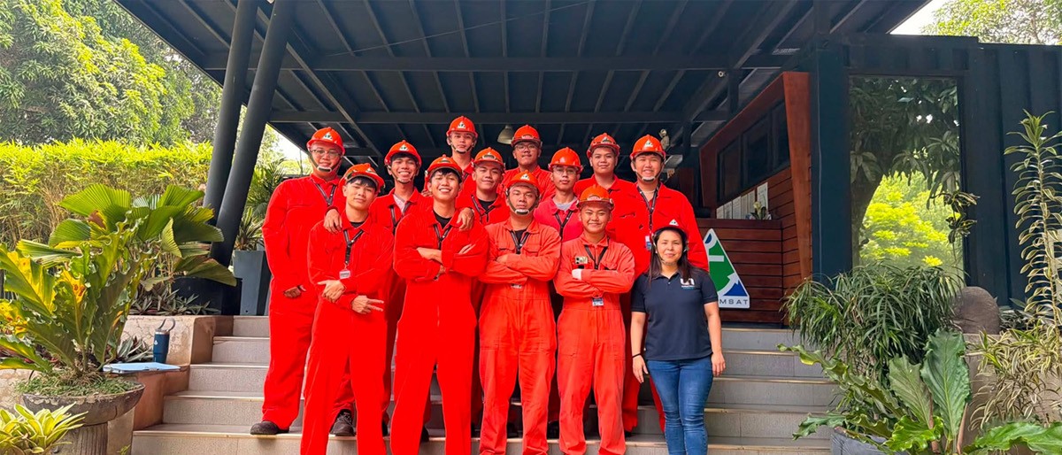 PHILCAMSAT conducts Cadet Resilience Program 02 | PTC Group of workers in red coveralls and orange helmets posing on outdoor steps with a woman in a polo shirt nearby outside a building.