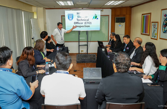 PHILCAMSAT successfully passes MARINA Accreditation-3 | PTC Presenter points to a screen during a briefing in a meeting room; attendees sit around a long table, watching the slide 'Technical Officer (TO) Inspection)'.