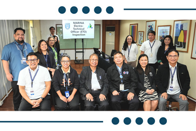 Twelve staff with lanyards posing for a group photo in a hallway; a sign behind them reads 'Marina Electro-Technical Inspection'.