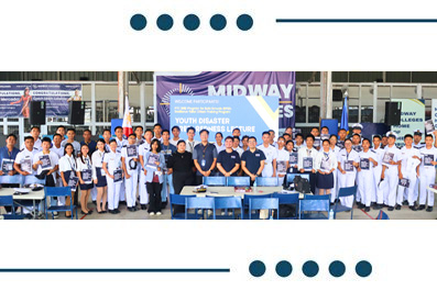 Group of students in white uniforms posing with teachers at a youth disaster preparedness event, banners visible in the background.
