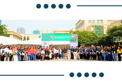 Large group of people posing for a group photo at an outdoor event with a green banner stage in the background.
