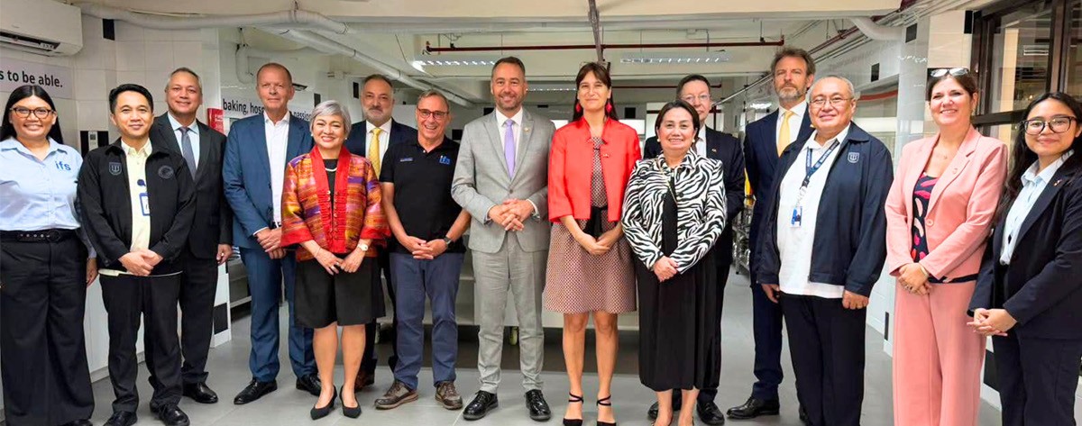 PTC and PHILCAMSAT join MARINA 02 | PTC Group of diverse professionals in business and smart casual attire posing for a group photo in a bright industrial workspace.