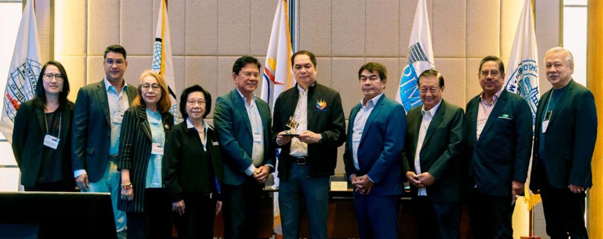 PTCs Capt Ronald Enrile supports DMW 02 | PTC Group of professionals in business attire posing for a photo at a formal event, with a trophy held by one person and flags in the background.