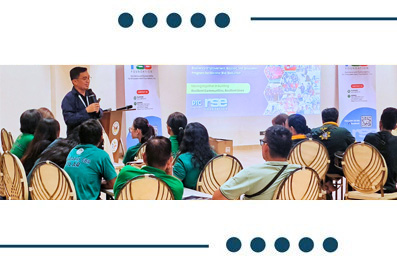 Speaker presenting to a seated audience in a conference room with a projected slide behind them, giving a talk at a workshop. (informative)