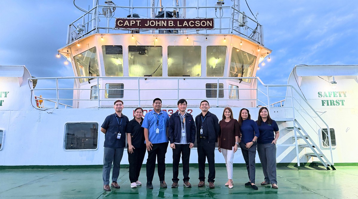 Strengthening onboard excellence 02 | PTC Eight crew members stand in a line on a ship’s deck, posing in front of the captain’s bridge with a lit railing sign CAPT. JOHN B. LACSON.