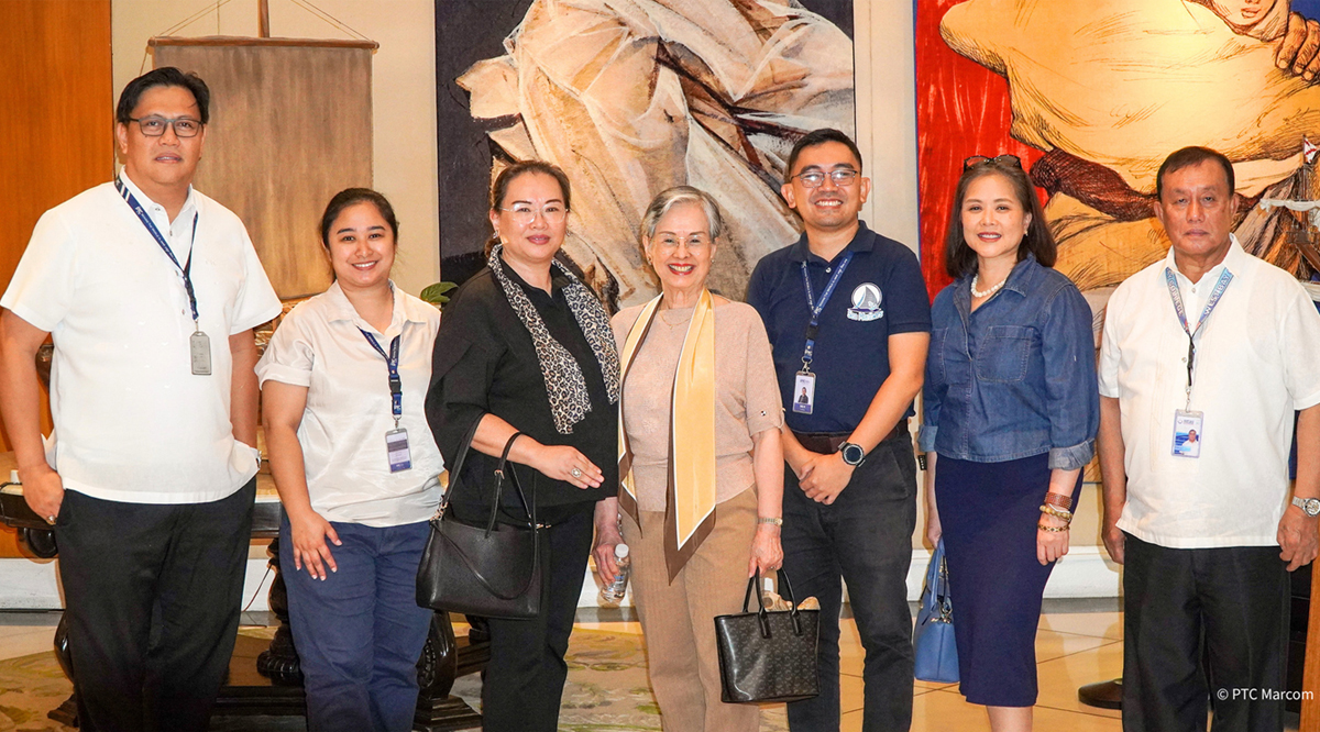 next generation of Global Maritime-2 | PTC Eight adults stand together posing for a group photo in a lobby with large artworks in the background, all wearing lanyards or badges.